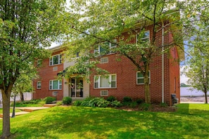 A two-story brick building with a front entrance, a small porch, and a well-maintained lawn.