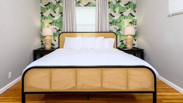 Una cama con cabecera trenzada, dos mesitas de noche con lámparas y una pared con estampado de pájaros verdes y blancos.
