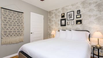 Un dormitorio con una cama, dos mesitas de noche con lámparas, una puerta y una pared decorada con marcos.