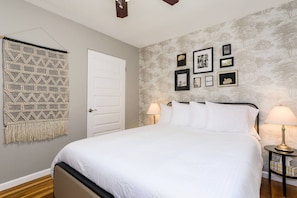 A bedroom with a bed, two bedside tables with lamps, a door, and a wall with framed pictures.