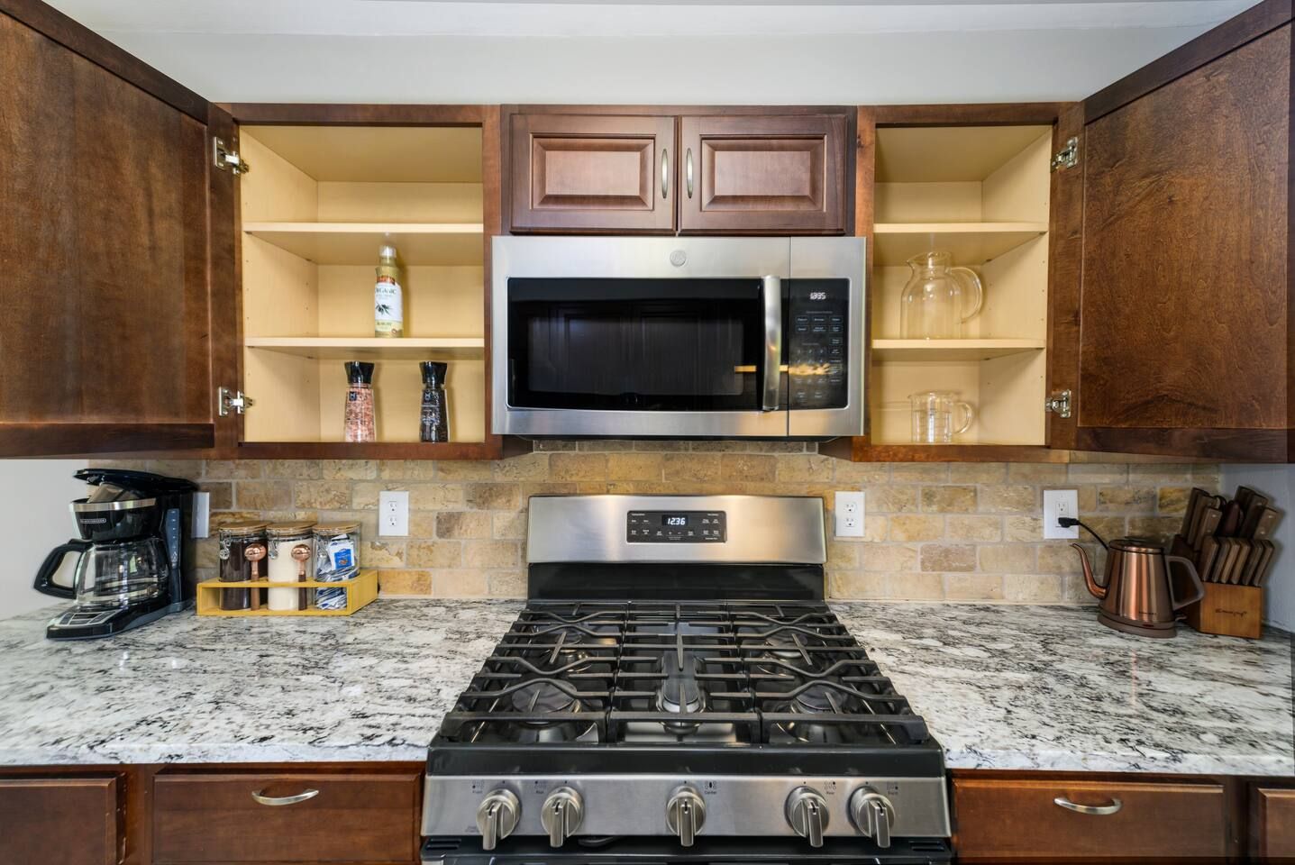 A kitchen with a gas stove, stainless steel microwave, wooden cabinets, and granite countertops.