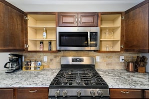 A kitchen with a gas stove, stainless steel microwave, wooden cabinets, and granite countertops.