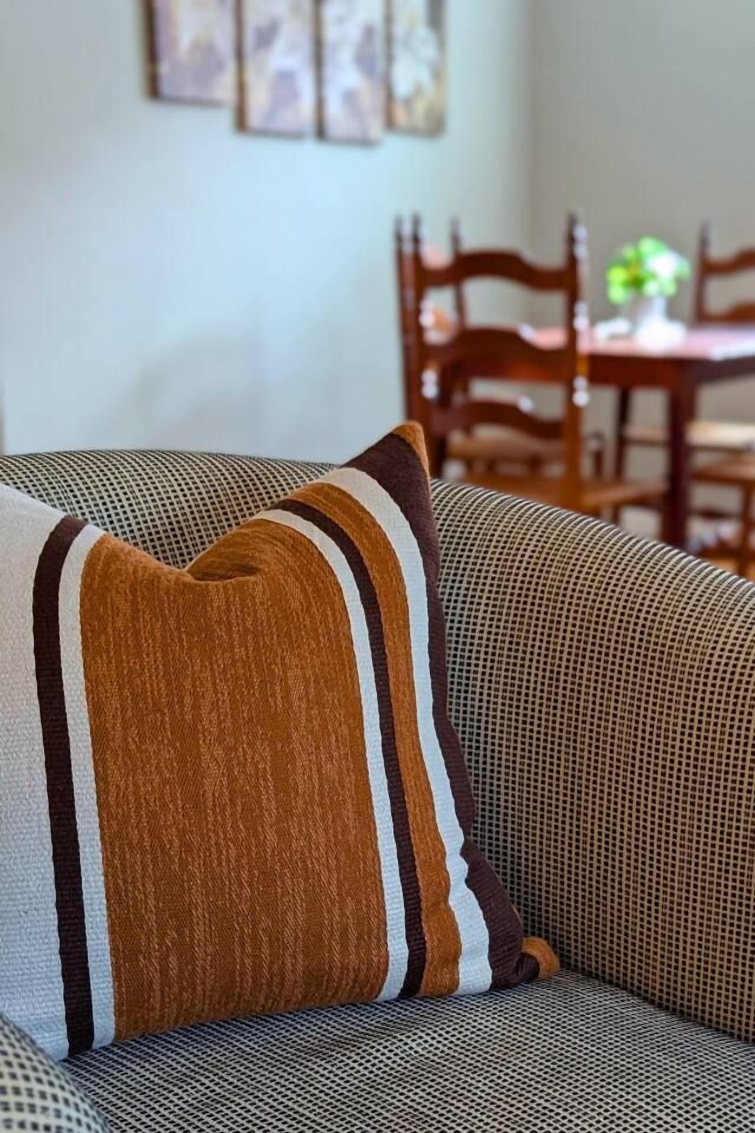A sofa with a patterned cushion and a dining area in the background.