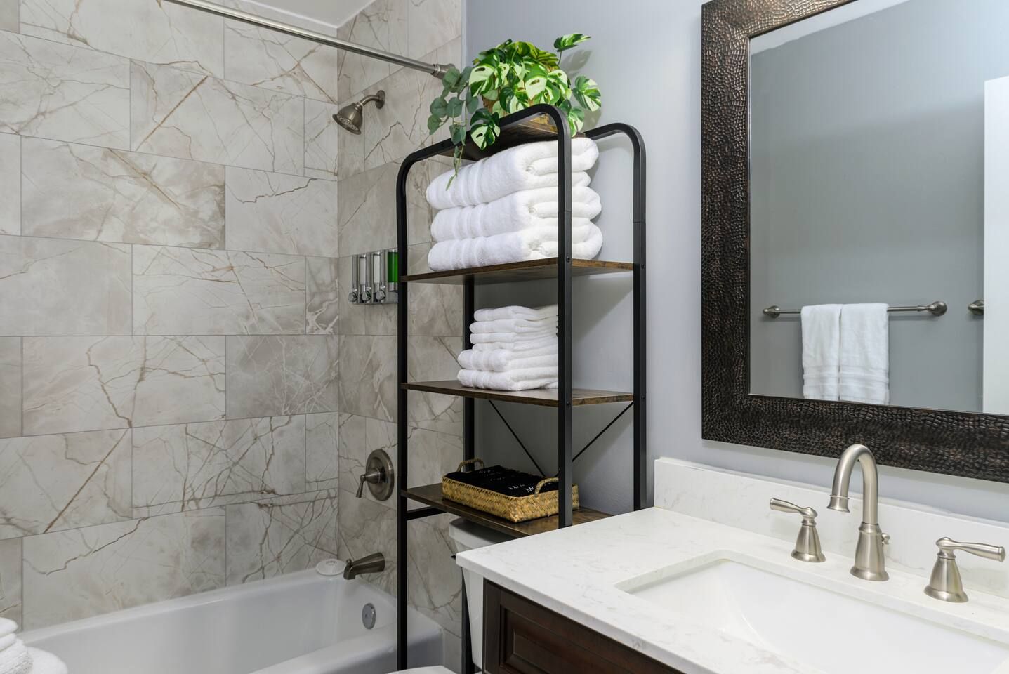 A bathroom with a marble wall, a bathtub, a sink with two faucets, and a towel rack with folded towels.