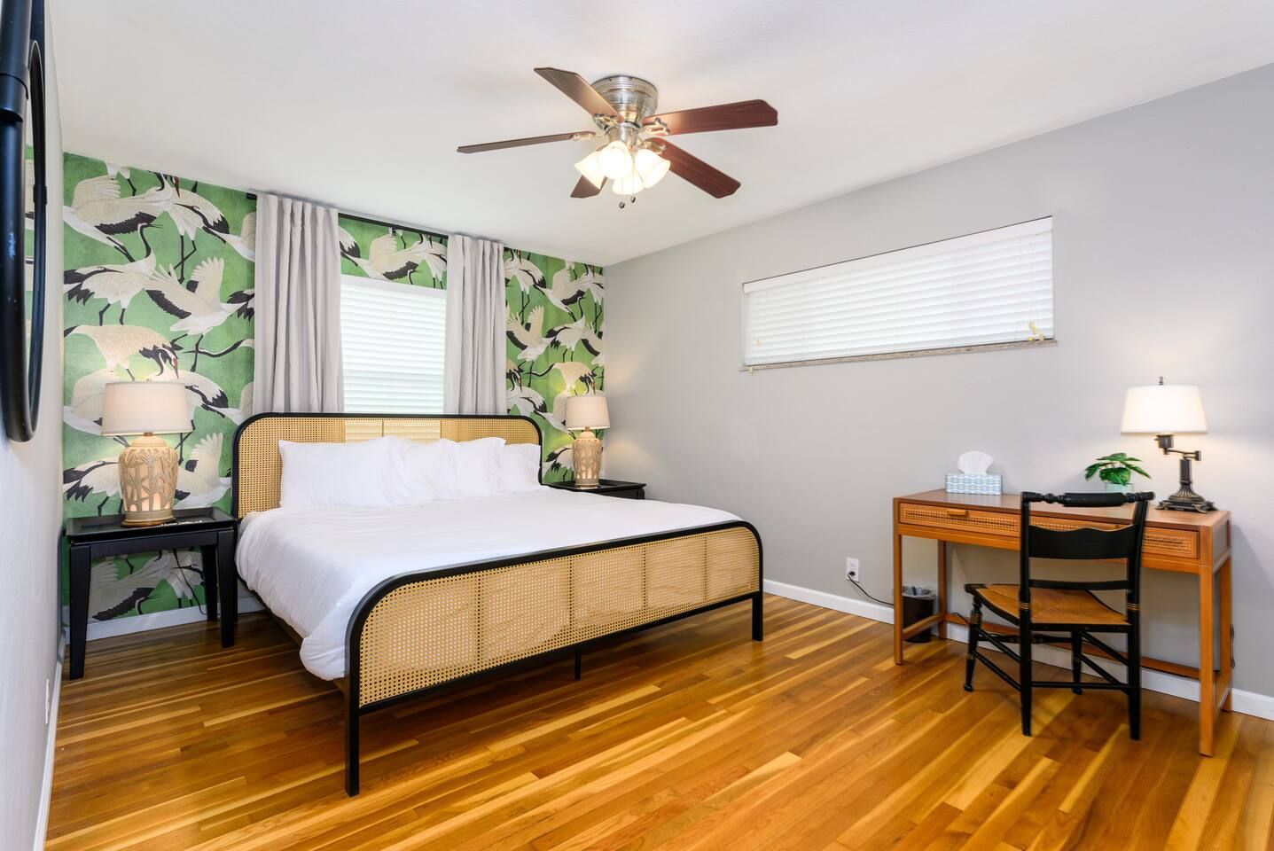 A bedroom with a bed, a desk, a chair, a ceiling fan, and a window with blinds.