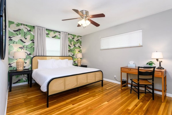 A bedroom with a bed, a desk, a chair, a ceiling fan, and a window with blinds.