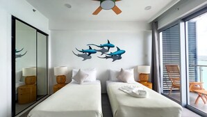 Habitació d'hotel amb dos llits, un ventilador de sostre, una finestra gran i un balcó amb mobles de jardí.