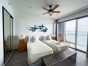 A hotel room with two beds, a ceiling fan, a large window with a view, and a wooden bench.