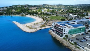 Eine Küstenlandschaft mit Strand, einem Felsenmole und einem modernen Gebäude mit Parkplatz.
