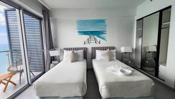 A hotel room with two beds, a large window, a balcony, and a wall art depicting a seascape.