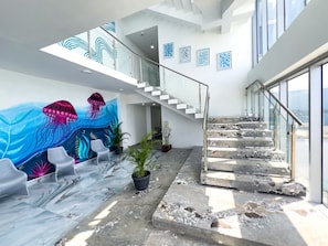 A modern interior with a staircase, seating area, and a mural. - Boardwalks - A Sky Harbour Oceanfront Twin Suite (Montego Bay)