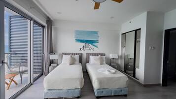 A hotel room with two beds, a ceiling fan, a large window, and a view of the outdoors.