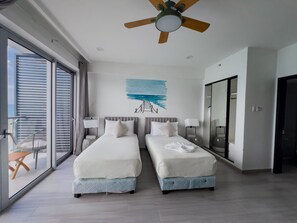 Ein Hotelzimmer mit zwei Betten, einem Deckenventilator, einem großen Fenster und Blick ins Freie.