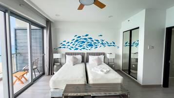 A hotel room with two beds, a ceiling fan, a large window with blinds, a balcony with a table and chairs, and a wall mural of fish.