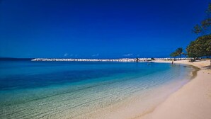 Una platja amb aigua cristal·lina, un tram de sorra i una roca a la distància.