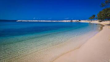 A beach with clear water, a sandy shore, and a rocky outcrop in the distance.