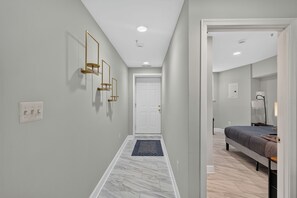 A hallway with a door, a bed, and a lamp in a bedroom. - Private DC 2BR Suite Near Shaw + NoMa Metro, Downtown, Union Market + Howard U (Washington)