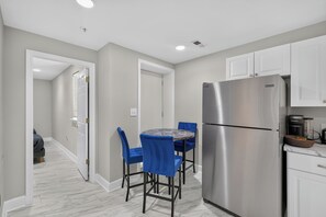 A modern kitchen with a stainless steel refrigerator, a dining table with blue chairs, and a hallway leading to another room. - Private DC 2BR Suite Near Shaw + NoMa Metro, Downtown, Union Market + Howard U (Washington)