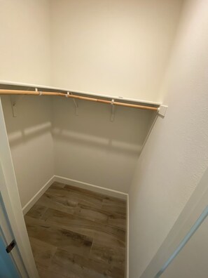 Ein begehbarer Kleiderschrank mit Kleiderstange, weißen Wänden und Holzboden.