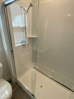 Eine begehbare Dusche mit Glaswänden, einer Handbrause und einem am Wand montierten Wasserhahn.