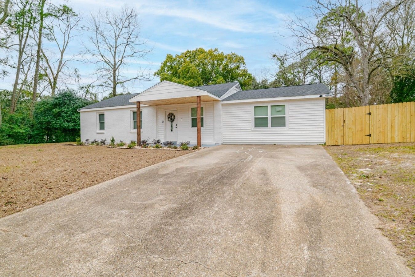 Une maison de plain-pied avec un porche à l’avant, une allée et une clôture en bois.