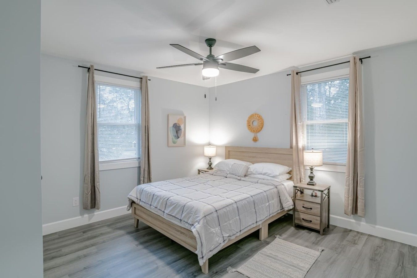 Une chambre à coucher avec un lit, deux tables de chevet, un ventilateur de plafond et une fenêtre avec des rideaux.