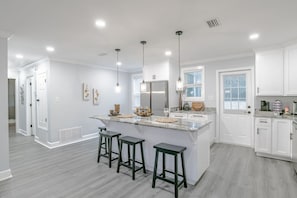 A modern kitchen with a central island, bar stools, pendant lighting, and white cabinetry. - White House on University (Mobile)