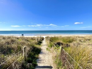 A sandy pathway leading to a beach with a clear sky. - Big Beachside Bach/1 min to Sand & Sea/Sleeps 10 (Tauranga)