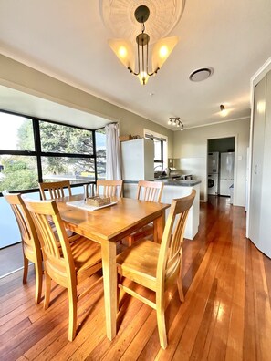 A spacious kitchen with a dining area, large windows, and a modern chandelier. - Big Beachside Bach/1 min to Sand & Sea/Sleeps 10 (Tauranga)