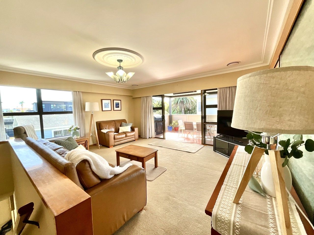 A spacious living room with a sofa, coffee table, and a television. There is a balcony with a view of the city.