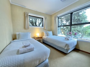 A hotel room with two beds, a nightstand, and a window with curtains. - Big Beachside Bach/1 min to Sand & Sea/Sleeps 10 (Tauranga)