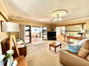 A spacious living room with a sofa, coffee table, and a television. - Big Beachside Bach/1 min to Sand & Sea/Sleeps 10 (Tauranga)