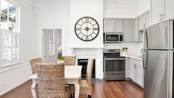 Una cocina moderna con comedor, que incluye un reloj de pared grande, electrodomésticos de acero inoxidable y mobiliario de mimbre.
