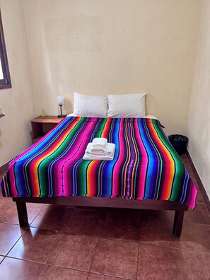 A bed with a colorful striped bedspread, white pillows, and a small bedside table with a lamp and a bottle. - 2-bedroom apartment in welcoming Antigua neighborhood. (Antigua)