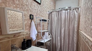 Casa de banho com lavatório, sanita, cortina de chuveiro e uma prateleira com artigos de higiene pessoal.