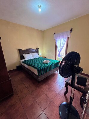 A bedroom with a bed, a nightstand, a wall-mounted fan, and a window with curtains. - 2-bedroom apartment in welcoming Antigua neighborhood. (Antigua)