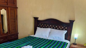 Uma cama com colcha listrada em verde e azul, travesseiros brancos e cabeceira de madeira.