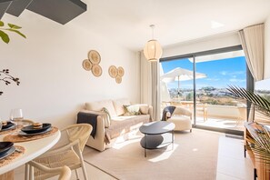 Ein modernes Wohnzimmer mit Sofa, Esstisch, Stühlen, einem Balkon mit Aussicht und dekorativer Wandkunst.