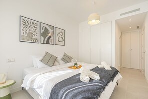 A hotel room with a bed, pillows, a bedside table, a lamp, a tray with wine bottles and a croissant, and artwork on the wall. - Bahia La Cala Paradise And Sunshine, La Cala de Mijas, Spain (La Cala de Mijas)