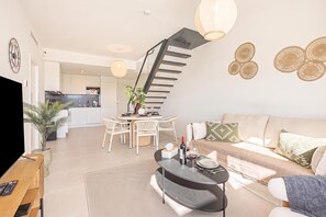 A modern living room with a sofa, coffee table, and dining area. There is a staircase leading to an upper level. - Bahia La Cala Paradise And Sunshine, La Cala de Mijas, Spain (La Cala de Mijas)