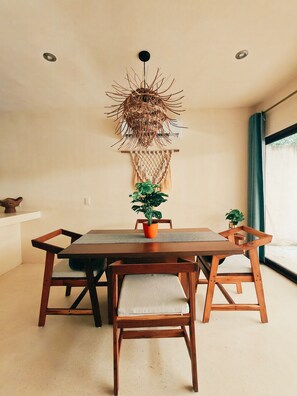 A dining area with a wooden table, chairs, a hanging macrame wall decoration, and a potted plant. - Peaceful Luxury Ground-Floor Retreat, 2BR, 2BA, Selva Norte Tulum (Tulum)
