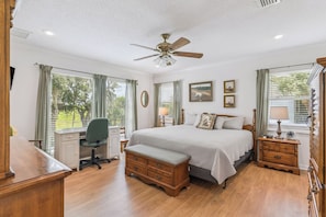 A bedroom with a bed, desk, chair, and a ceiling fan.