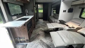 A compact RV interior with a kitchenette, a seating area with cushioned seats, and a window providing a view of greenery. - Luxury Mercedes 25 Foot RV w/ Full Bathroom + WiF/TV close to the Poconos (Blairstown)