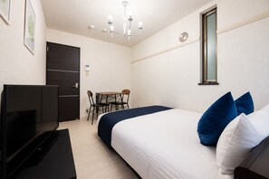 Una camera d'albergo con un letto, una scrivania, una sedia, una TV, un lampadario e un orologio appeso al muro.