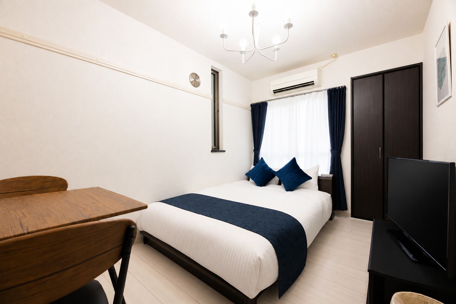 A hotel room with a bed, a desk, a television, and an air conditioning unit.