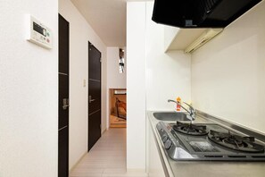A narrow hallway leading to a kitchen with a gas stove and a sink. - Biancolina (Fukuoka City)