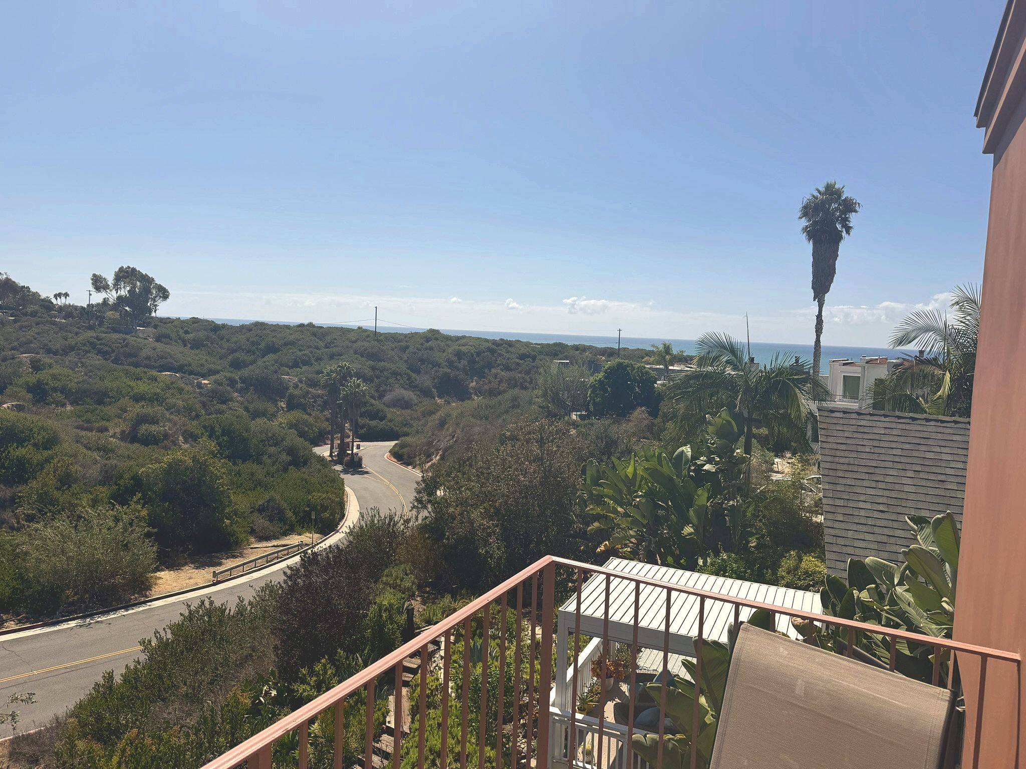 Un balcon offrant une vue sur une route sinueuse qui traverse une zone boisée et mène à la côte.
