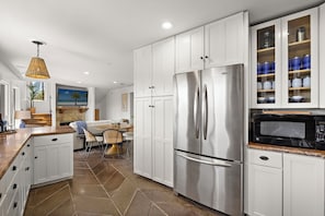 A modern kitchen with white cabinetry, a stainless steel refrigerator, a microwave, and a dining area with a table and chairs. - Quiet Retreat w/ Coastal View + Walk to Beach (San Clemente)