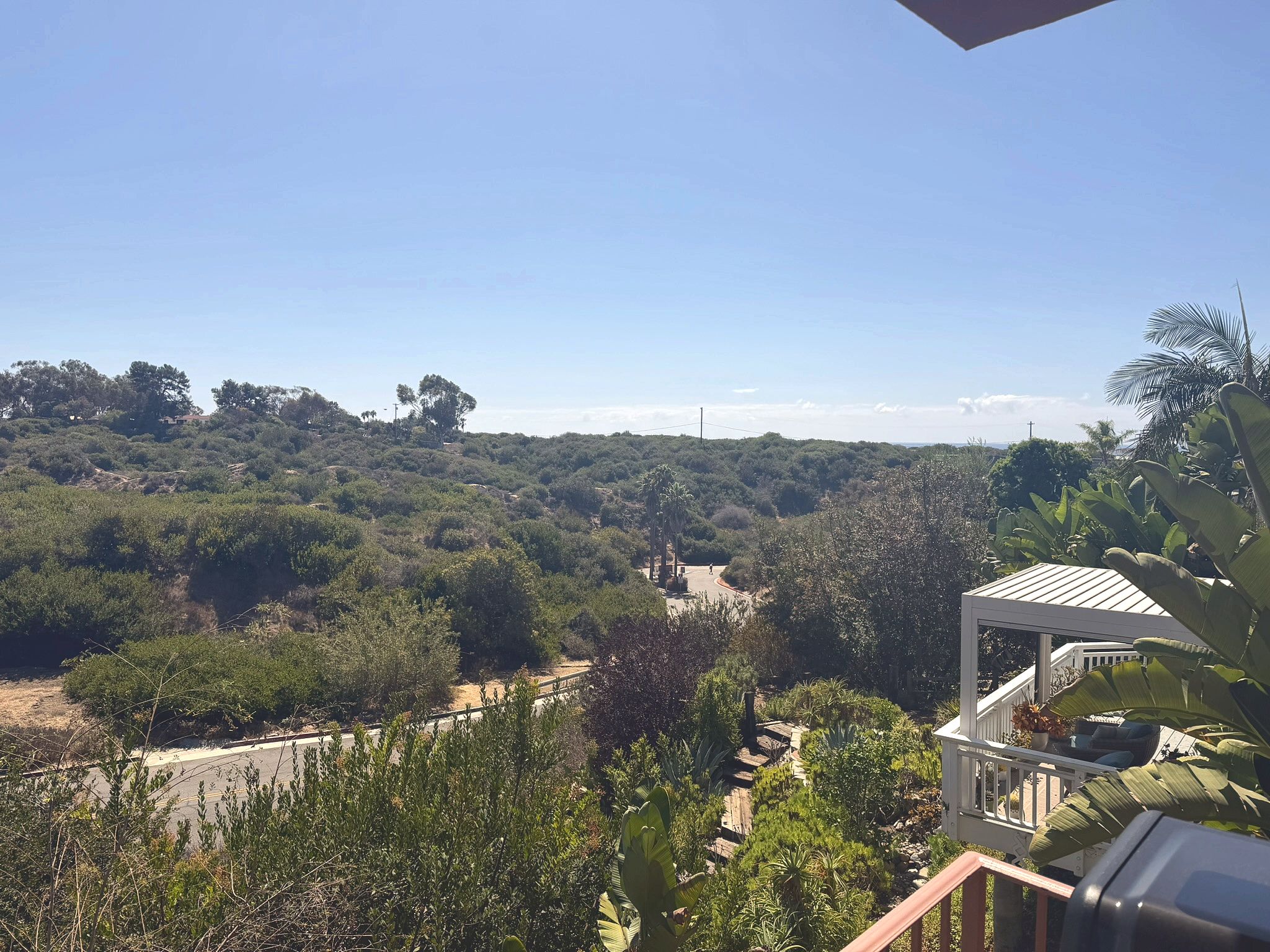 Ein Balkon mit Blick auf eine hügelige Landschaft, einen gepflasterten Weg und ein weißes Gebäude mit Dach.