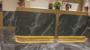 A reception desk with a marble top and a modern design, featuring a wall-mounted light fixture and potted plants. - Majestic Park Inn (Vapi)